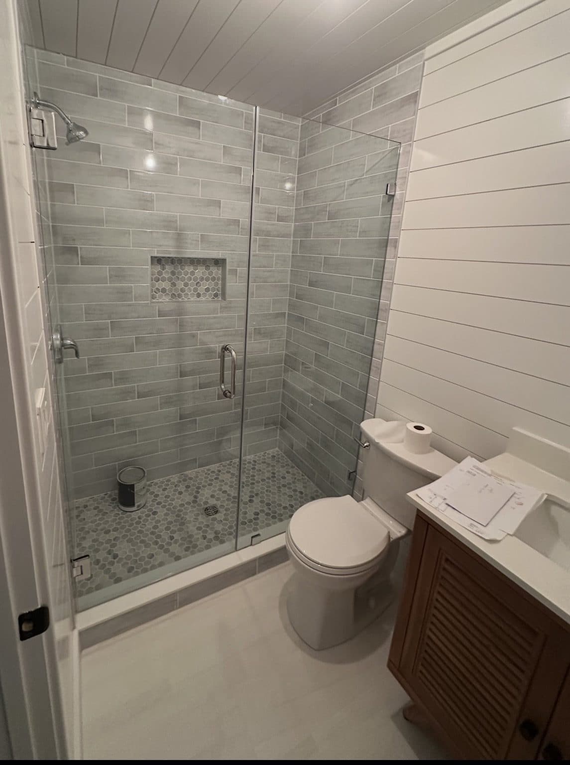 Finished walk-in shower in grey plank tile with a hex mosaic floor and frameless glass