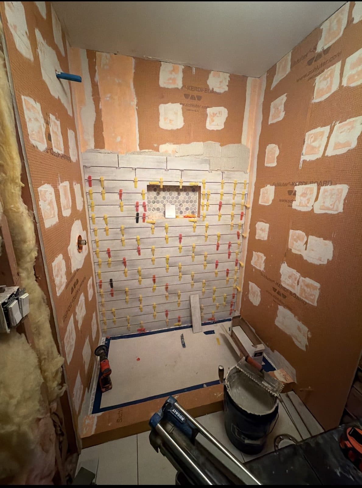 Shower walls in orange waterproof board with every seam banded, the pan taped off and tile going up on leveling clips
