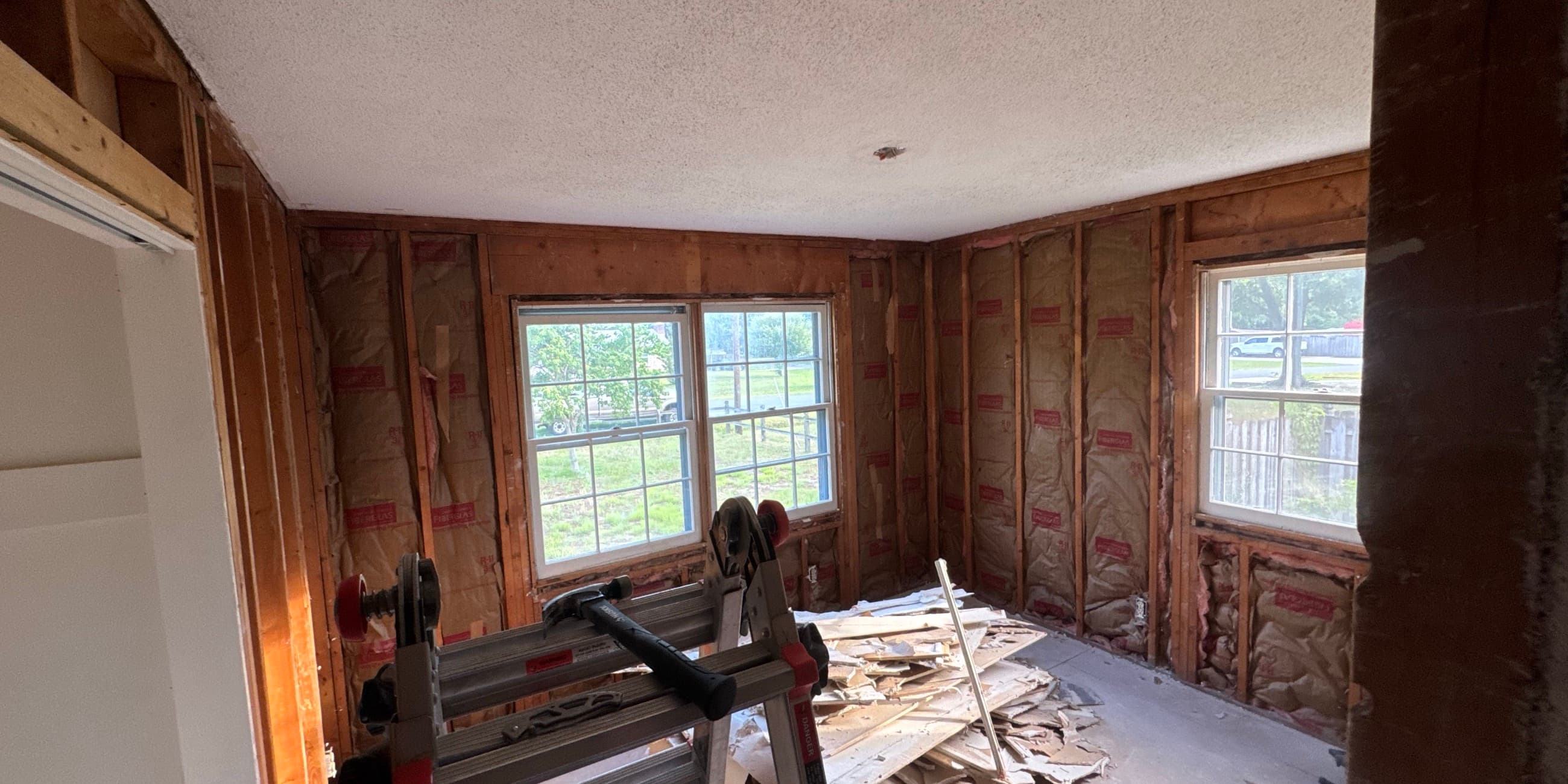 Bedroom stripped to bare studs and insulation with debris on the subfloor