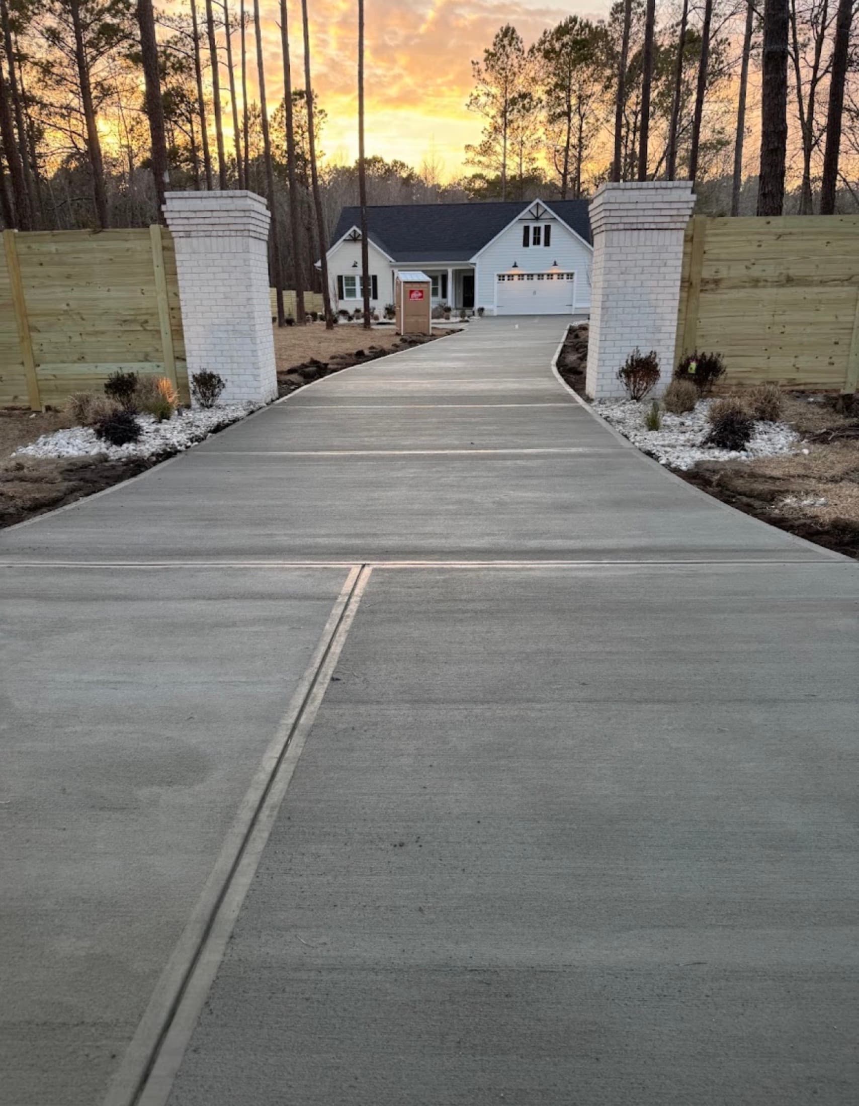 New concrete driveway between brick entry columns at sunset