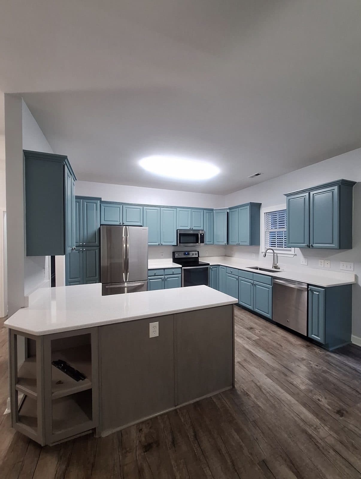 Refinished teal kitchen cabinets with white counters, a grey island and stainless appliances